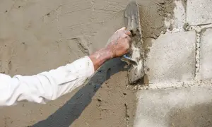 Ręka w białej koszuli tynkuje ścianę z bloczków betonowych kielnią. Proces jak zrobić baranek cementowy w praktyce.