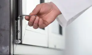 Dłoń używa klucza imbusowego do regulacji zawiasu okna, pokazując, jak otworzyć okno plastikowe bez klamki.