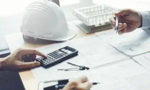 Inżynierowie przy biurku, kalkulator i szkice pomagają ustalić, jak obliczyć kubaturę pomieszczenia.
