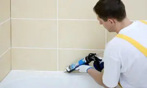 Fachowiec nakłada białą fugę epoksydową Mapei na styku wanny i beżowych płytek, zapewniając estetyczne i szczelne wykończenie.