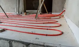 Czerwone rurki ogrzewania podłogowego ułożone na styropianie na podłodze w trakcie budowy.
