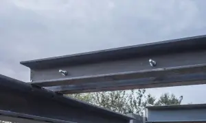 Stalowe belki stropowe połączone śrubami, pokazujące jak wzmocnić belki stropowe. Widok na niebo i drzewa w tle.
