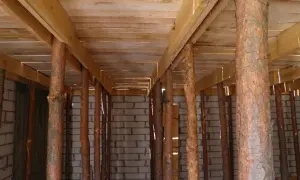 Drewniane stemple pod stropem, tworzące rusztowanie. W tle ściana z pustaków.