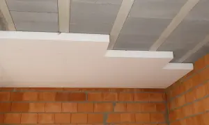 Płyty styropianowe montowane pod betonowym stropem to sposób, jak ocieplić strop. Widoczne ceglane ściany.