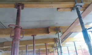 Wzmocnienie stropu drewnianego w starym domu: podparcie betonowej płyty stropowej za pomocą stalowych podpór budowlanych i drewnianych belek.