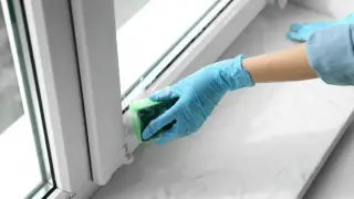 Ręka w niebieskiej rękawiczce czyści parapet gąbką. Dowiedz się, jak usunąć taśmę ze szkła, aby okna lśniły.