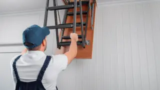 Fachowiec montuje schody strychowe, pokazując, jak uszczelnić schody strychowe, by uniknąć strat ciepła.
