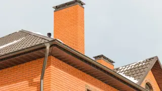 Nowoczesny dom z cegły, z widocznym kominem i dachem. Dowiedz się, jak obudować komin wewnątrz domu, aby był estetyczny i funkcjonalny.