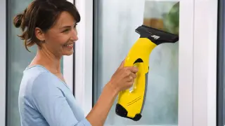 Uśmiechnięta kobieta pokazuje, jak używać myjki do okien Karcher do czyszczenia zaparowanej szyby.