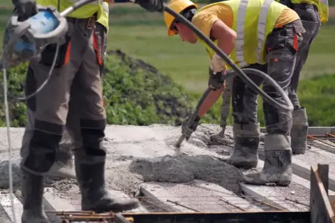 Budowlańcy w kamizelkach i kaskach wylewają beton na strop. Prawidłowe wykonanie to klucz do tego, jak dbać o świeży strop.