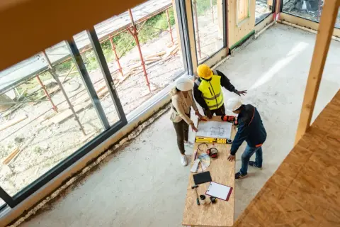 Architekci omawiają projekt, ustalając, ile kosztuje strop drewniany. Na stole plany, narzędzia i próbki materiałów.