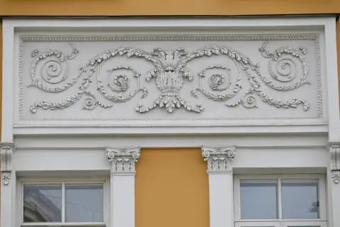 Eleganckie sztukaterie nad oknami to inspiracja, jak ozdobić ścianę zewnętrzną. Wzory liści i winogron dodają klasy.