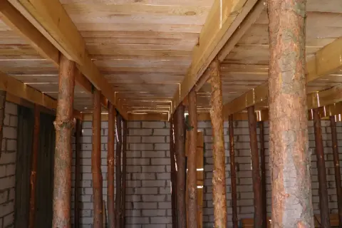 Drewniane stemple pod stropem, tworzące rusztowanie. W tle ściana z pustaków.