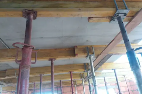 Wzmocnienie stropu drewnianego w starym domu: podparcie betonowej płyty stropowej za pomocą stalowych podpór budowlanych i drewnianych belek.