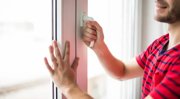 Mężczyzna w czerwonej koszulce z paskami próbuje otworzyć plastikowe okno od zewnątrz.