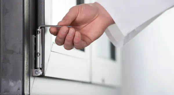 Dłoń używa klucza imbusowego do regulacji zawiasu okna, pokazując, jak otworzyć okno plastikowe bez klamki.