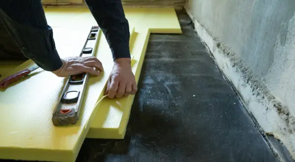 Ręce układają żółty styropian pod wylewkę, używając poziomicy. Unikaj błędów przy układaniu styropianu pod wylewkę.
