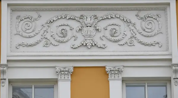 Eleganckie sztukaterie nad oknami to inspiracja, jak ozdobić ścianę zewnętrzną. Wzory liści i winogron dodają klasy.