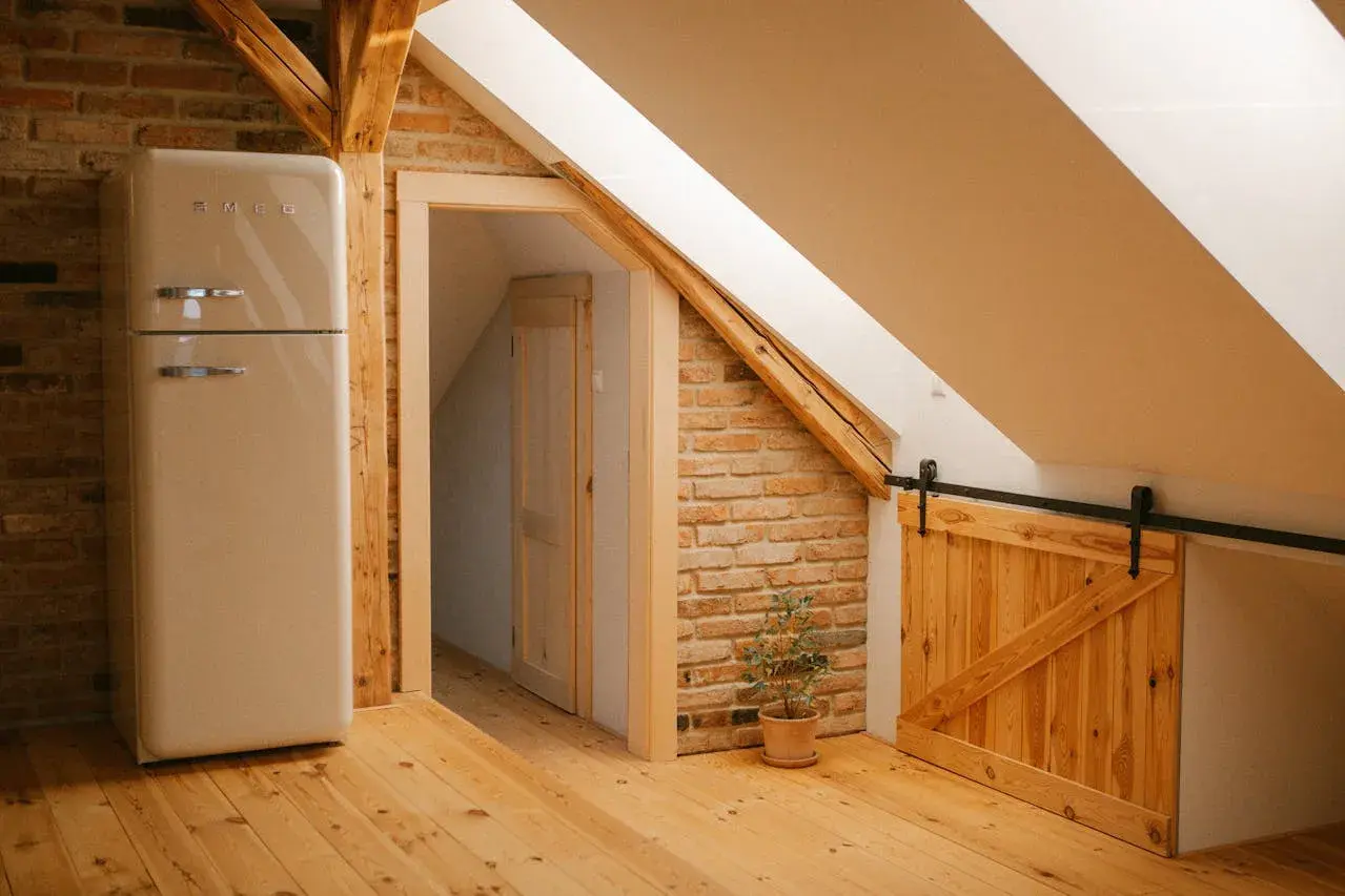 Kremowa lodówka Smeg stoi na drewnianej podłodze. W tle widać drzwi i ceglaną ścianę. Czy poddasze nieużytkowe to kondygnacja?