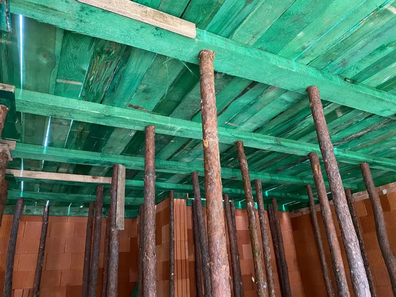 Widać wiele drewnianych słupów, co ile stemple pod stropem, podtrzymujących zielone deski stropowe.