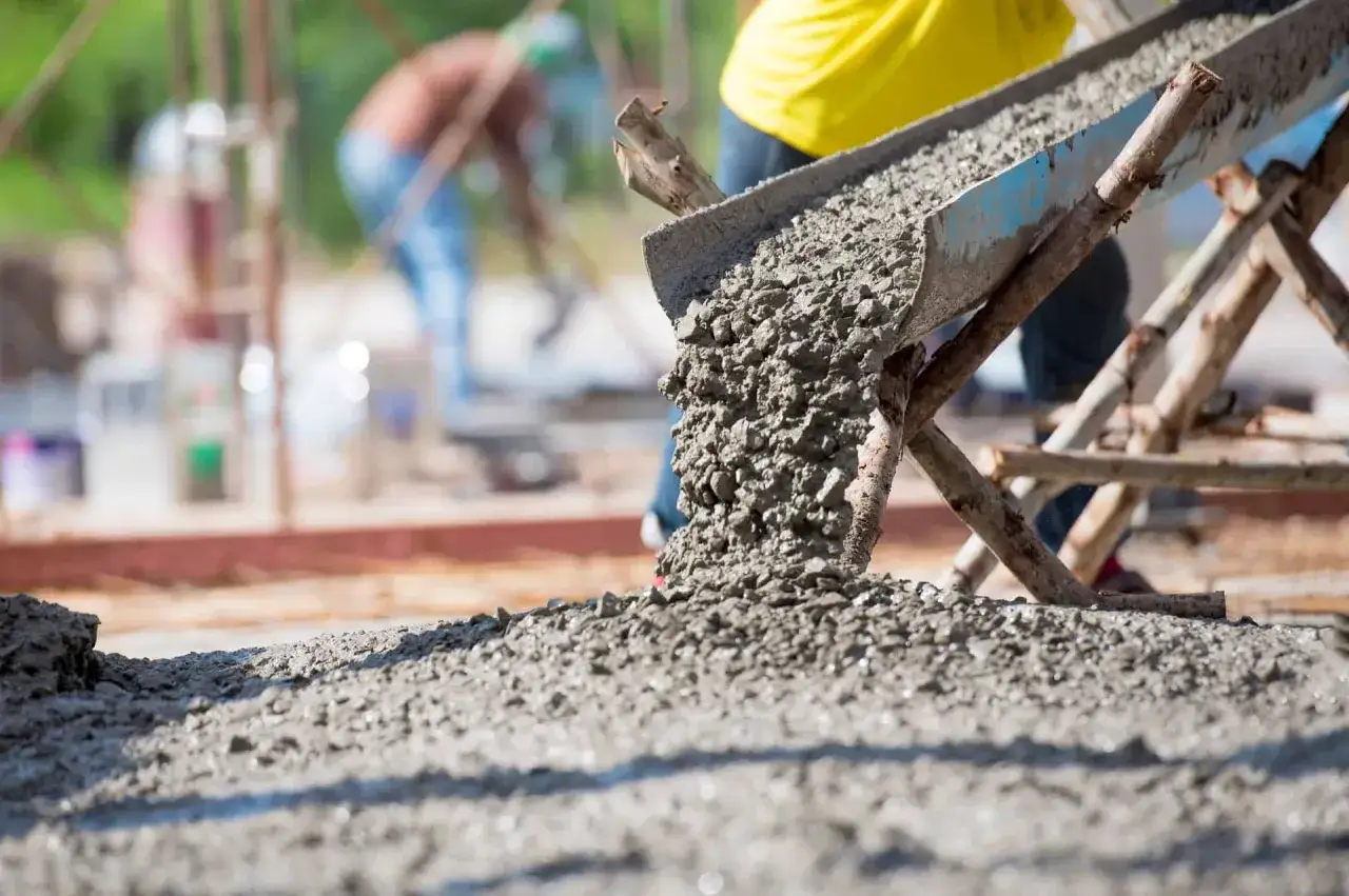 Beton wylewany z rynny na placu budowy. W tle pracownicy. Obrazek pomocny, by zrozumieć, jak obliczyć ilość betonu.