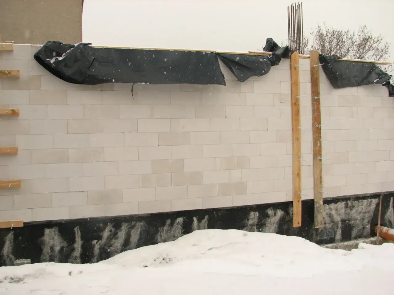 Ściana z bloczków z pianoklejem do murowania, zabezpieczona czarną folią przed zimnem i śniegiem.