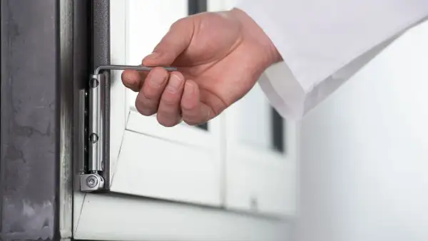 Dłoń używa klucza imbusowego do regulacji zawiasu okna, pokazując, jak otworzyć okno plastikowe bez klamki.