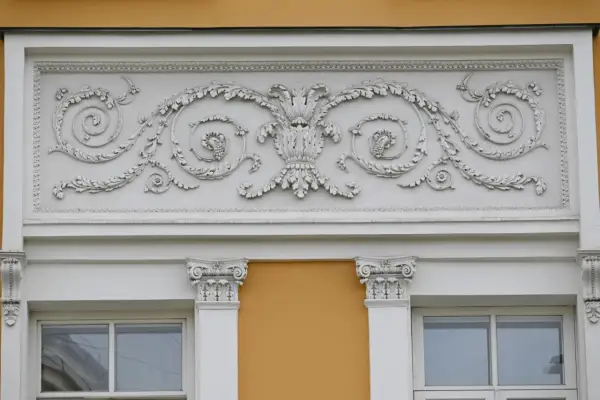Eleganckie sztukaterie nad oknami to inspiracja, jak ozdobić ścianę zewnętrzną. Wzory liści i winogron dodają klasy.