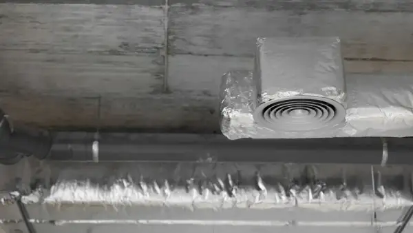 Ocieplanie rur wentylacyjnych na poddaszu folią aluminiową. Widoczny okrągły nawiewnik.